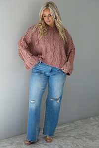 A woman wearing a mulberry oversized sweater paired with a pair of medium wash distressed denim, standing indoors against a white wall with white marble flooring. 