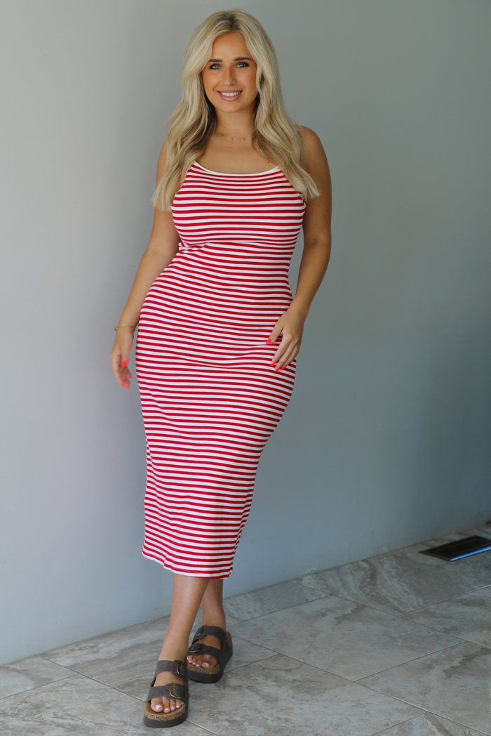 Woman in a red and white striped dress standing indoors against a white wall with white marble flooring. 
