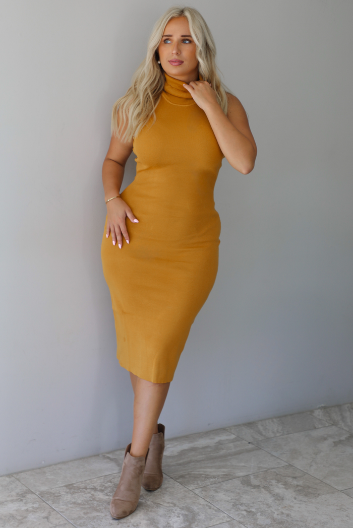 A woman wearing a marigold sleeveless midi dress with a high, turtle neckline, ribbed textured material, and is fitted, standing indoors against a white wall with white marble flooring. 
