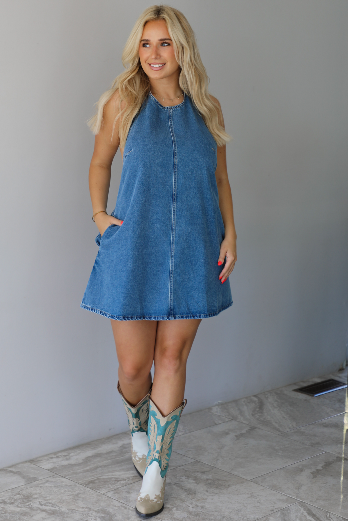 Woman wearing a denim blue dress indoors against a white wall with white marble flooring. 