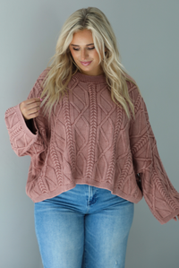 A woman wearing a mulberry oversized sweater paired with a pair of medium wash distressed denim, standing indoors against a white wall.