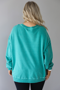 Woman wearing a teal oversized sweater with black leggings that have a slightly flared hem with split hem details in the front. The photo shows a closeup of the back of the sweater and has a white background. 