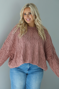 A woman wearing a mulberry oversized sweater paired with a pair of medium wash distressed denim, standing indoors against a white wall.