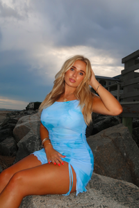 Woman wearing a blue mini dress sitting on rocks at the beach.