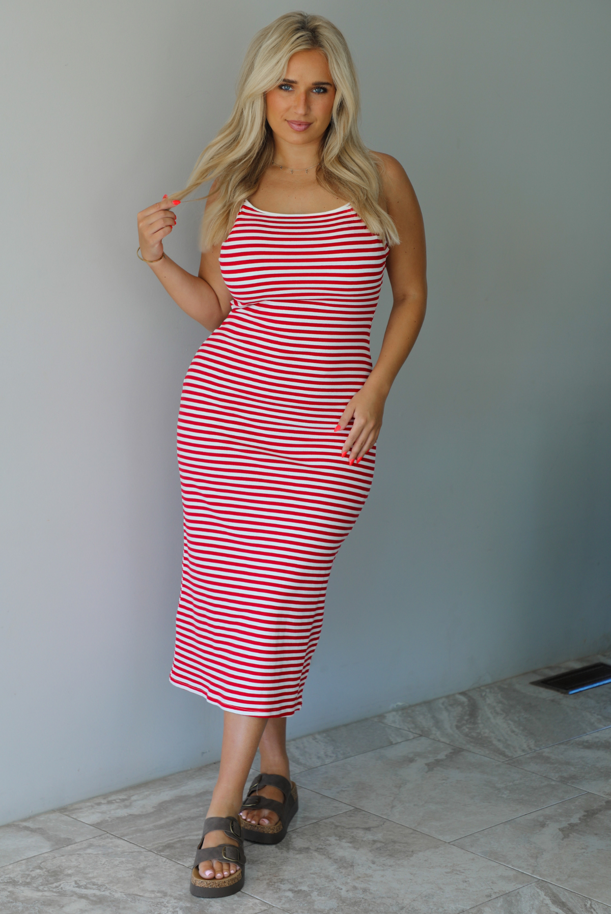 Woman in a red and white striped dress standing indoors against a white wall with white marble flooring. 