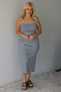 Woman wearing a navy and white striped fitted midi dress indoors against a white wall with white marble flooring. 