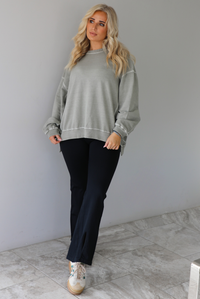 Woman wearing a tan oversized sweater with black leggings that have a slightly flared hem with split hem details in the front. The photo is taken indoors against a white wall with white marble flooring. 