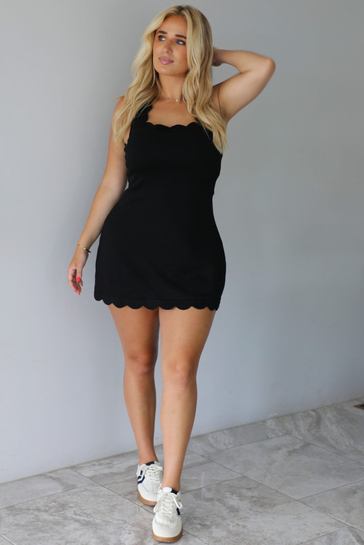Woman wearing a black mini dress indoors against a white wall with white marble flooring. 