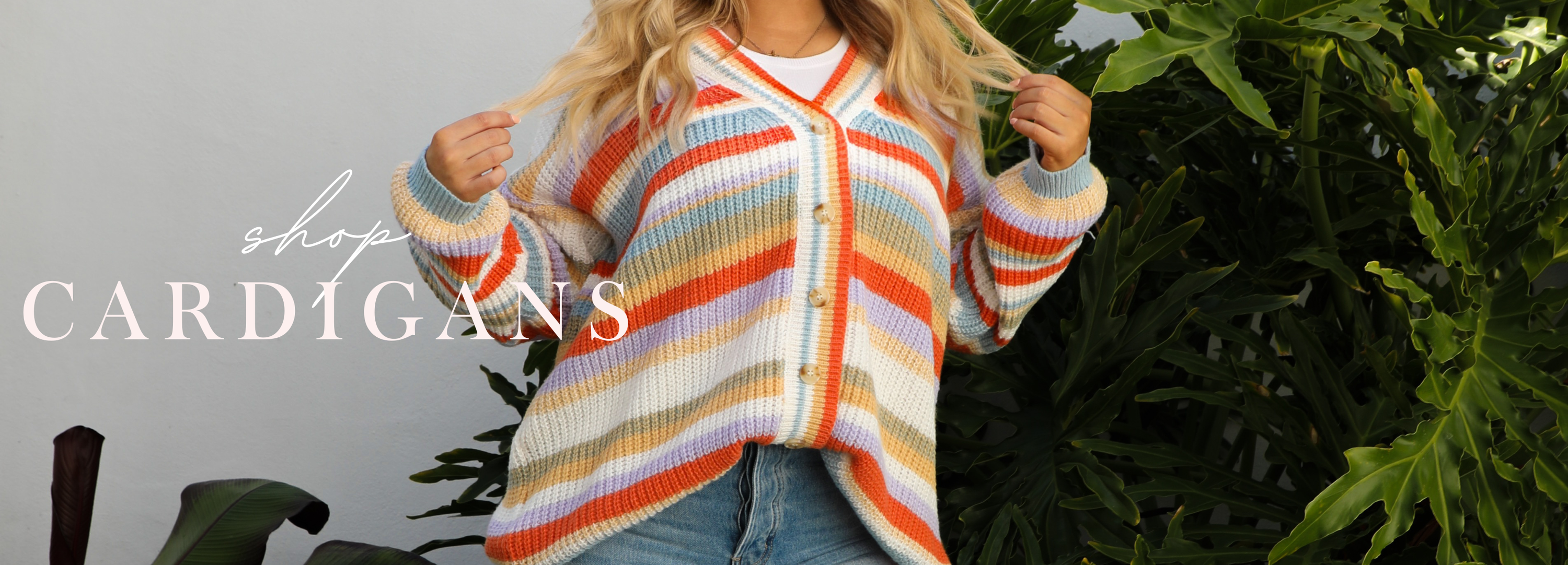 Person wearing a colorful striped cardigan with text 'Shop Cardigans' and plants in the background.