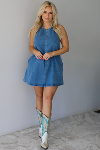 Woman wearing a denim blue dress indoors against a white wall with white marble flooring. 
