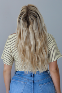 Woman wearing a pale yellow top with a taupe striped pattern with medium wash denim shorts indoors against a white wall. The photo shows the back of the top. 