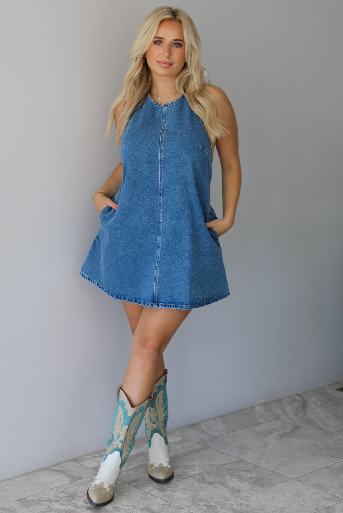 Woman wearing a denim blue dress indoors against a white wall with white marble flooring. 