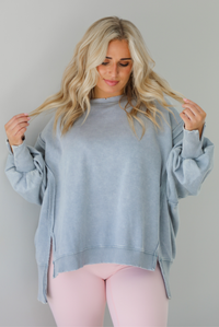 Woman wearing a grey colored oversized sweatshirt with exposed seam details and a high-low design with pink leggings. The photo is taken indoors against a white wall.