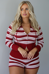 A woman modeling a matching red and white striped knit set with a front zipper, drawstring hood, paired with brown platform sandals, standing indoors against a white wall.