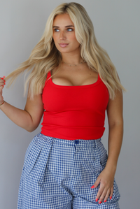 Woman wearing a red tank top high waisted navy and white plaid pants indoors against a white wall. The photo shows a closeup of the tank, which has a ribbed texture. 