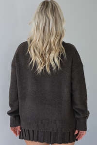 Woman wearing a dark brown sweater set featuring a turtle-neck sweater and a pleated skirt. The photo shows the back of the set. The photo is taken front of a white wall.