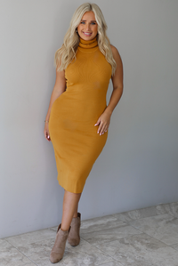 A woman wearing a marigold sleeveless midi dress with a high, turtle neckline, ribbed textured material, and is fitted, standing indoors against a white wall with white marble flooring. 