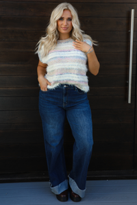 Woman model wearing a soft, striped sweater vest with dark wash denim jeans. The photo is taken outdoors against a dark brown wooden door. 