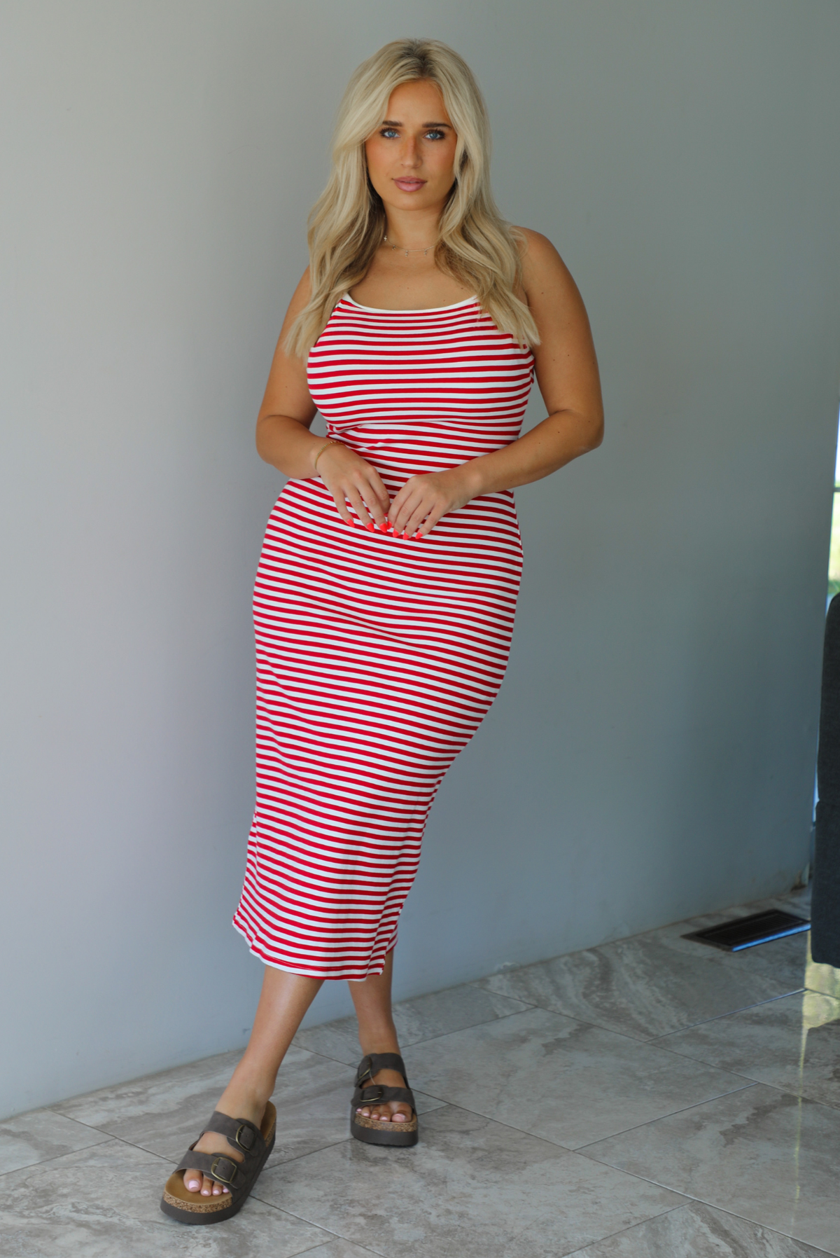 Woman in a red and white striped dress standing indoors against a white wall with white marble flooring. 