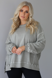 Woman wearing a tan oversized sweater with black leggings that have a slightly flared hem with split hem details in the front. The photo shows a closeup of the sweater and has a white background. 