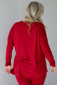 Woman wearing a red two piece set that features an oversized long sleeved top and fitted leggings. The photo shows a closeup of the back of the top. The photo is taken indoors against a white wall.
