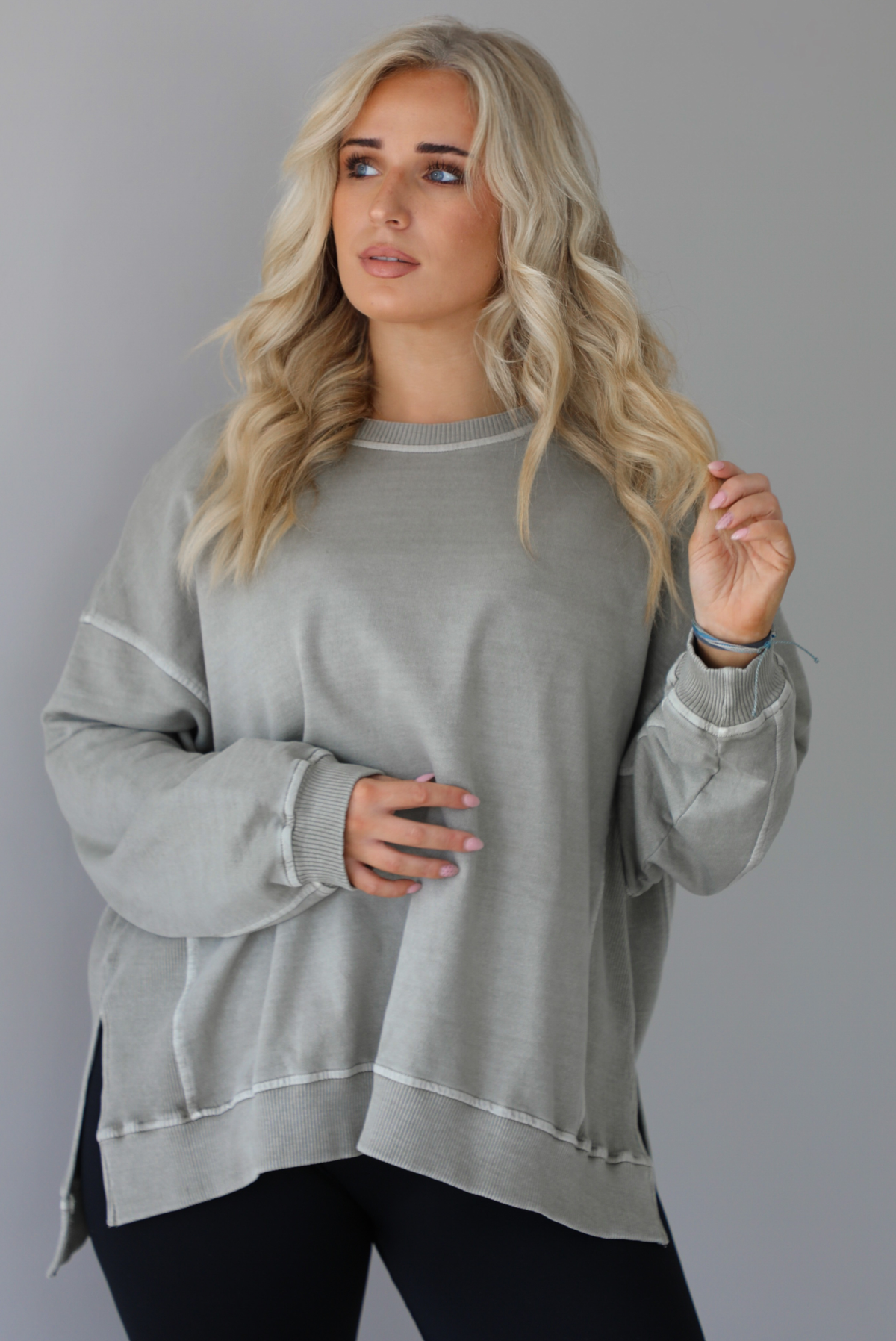 Woman wearing a tan oversized sweater with black leggings that have a slightly flared hem with split hem details in the front. The photo shows a closeup of the sweater and has a white background. 
