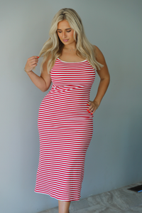 Woman in a red and white striped dress standing indoors against a white wall with white marble flooring. 