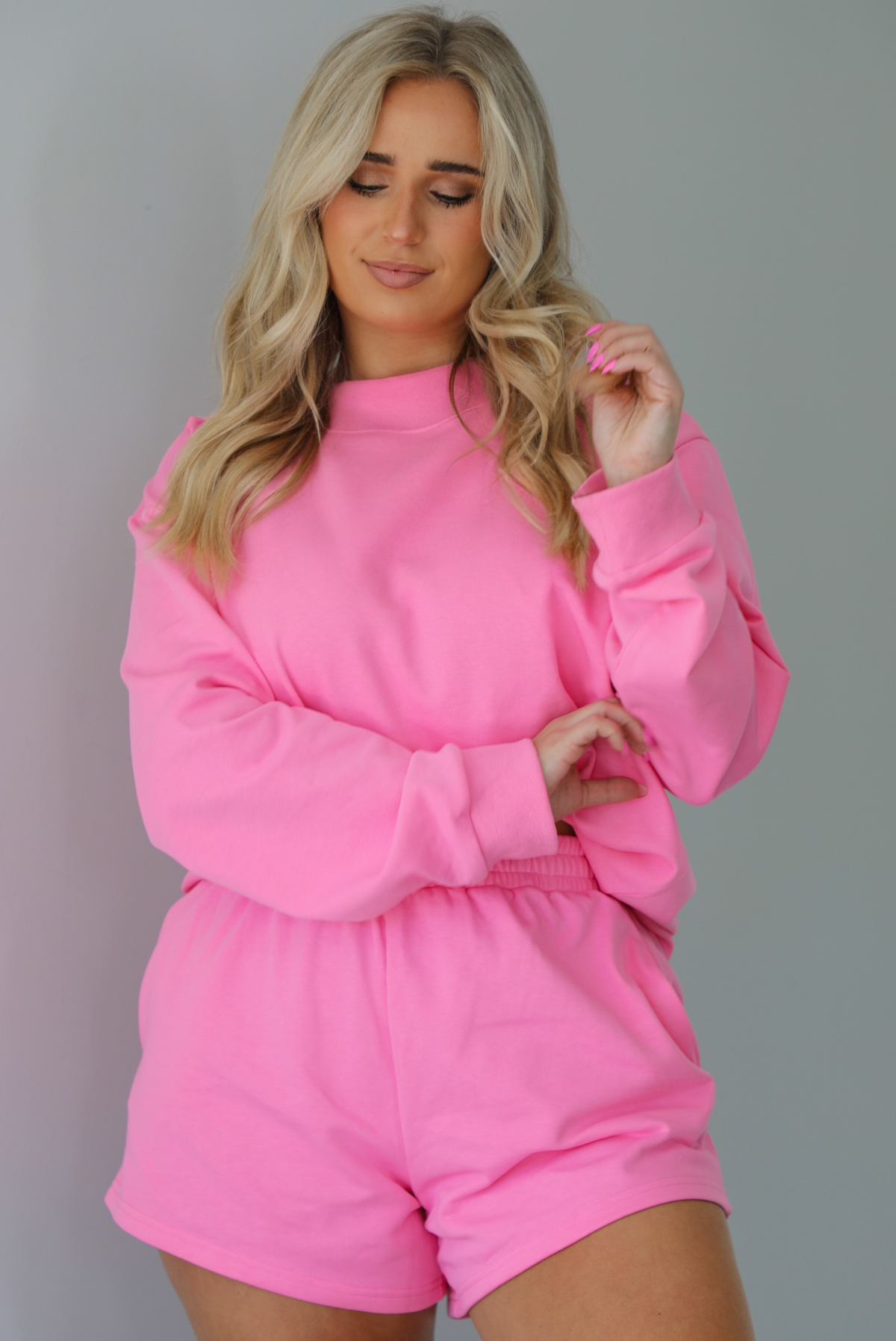 Woman wearing a hot pink two piece set featuring an oversized sweatshirt and high waisted shorts. The photo is taken indoors against a white wall and shows a closeup of the set.