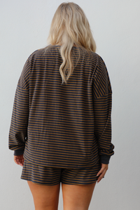 Close up of the back of a woman model wearing a brown and multi-colored striped pattern throughout. The set consists of an oversized top with quarter-button details and shorts. The photo is taken outdoors against a white wall. The photo showcases the full length of the top that stops mid-hip on our 5'7" model.
