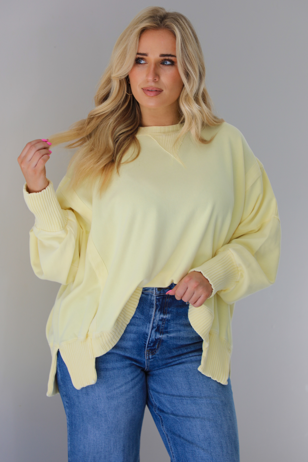 Woman wearing a pale yellow oversized sweater that's tucked into the front of dark wash denim.  The photo is taken indoors against a white wall.