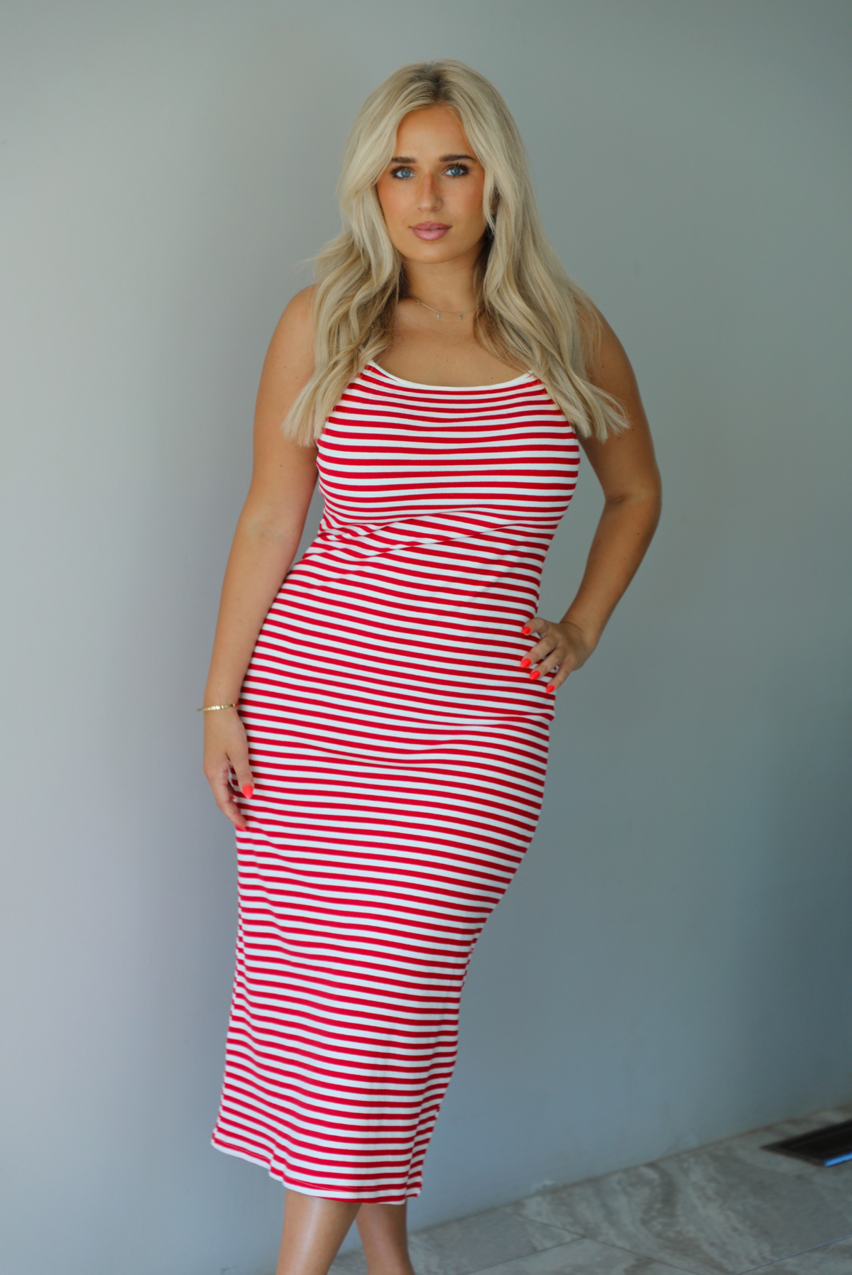 Woman in a red and white striped dress standing indoors against a white wall with white marble flooring. 