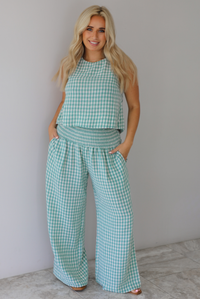 Woman wearing a mint and white gingham set with an oversized top and flared hem pants indoors against a white wall with white marble flooring. 