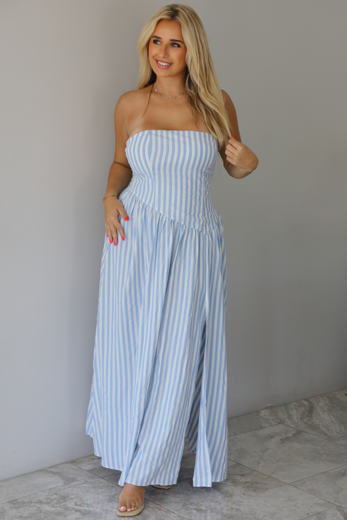 Woman wearing a blue and white striped strapless maxi dress indoors against a white wall with white marble flooring.