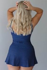 Woman wearing a navy and white polka for athleisure dress indoors against a white wall. The photo shows the back of the dress. 