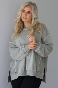 Woman wearing a tan oversized sweater with black leggings that have a slightly flared hem with split hem details in the front. The photo shows a closeup of the sweater and has a white background. 
