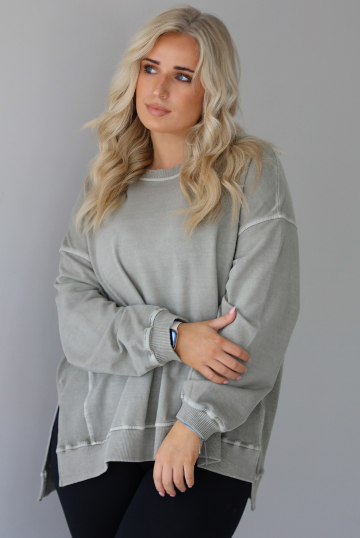 Woman wearing a tan oversized sweater with black leggings that have a slightly flared hem with split hem details in the front. The photo shows a closeup of the sweater and has a white background. 