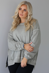 Woman wearing a tan oversized sweater with black leggings that have a slightly flared hem with split hem details in the front. The photo shows a closeup of the sweater and has a white background. 