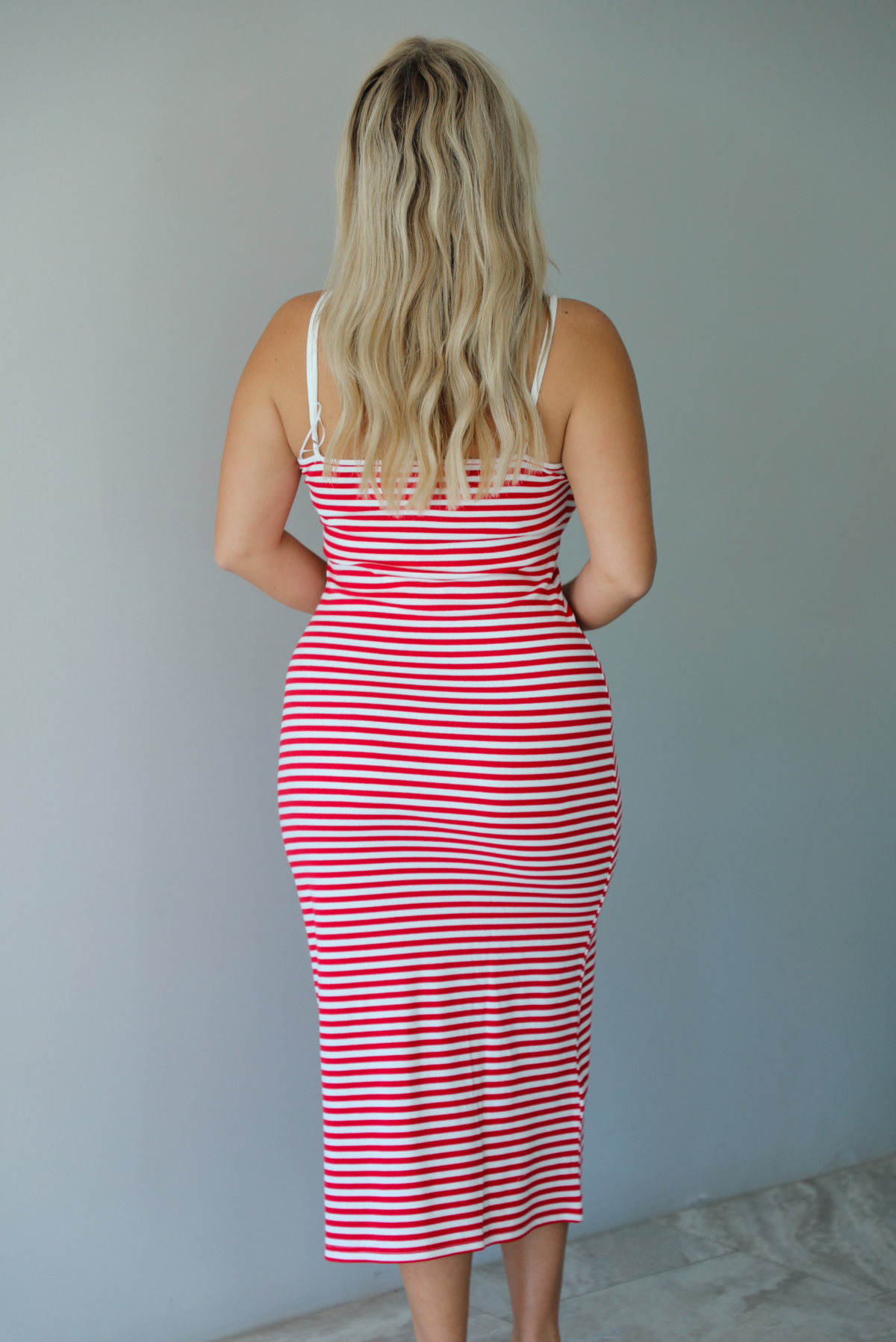 Woman in a red and white striped dress standing indoors against a white wall with white marble flooring. The photo shows the back of the dress. 