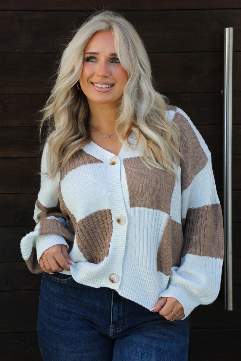 Close up of a woman model wearing a white and tan checkered patterned cardigan and dark wash denim. The cardigan has functional button closures in the front, is lightweight, and has a relaxed fit. 