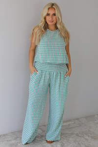 Woman wearing a mint and white gingham set with an oversized top and flared hem pants indoors against a white wall with white marble flooring. 