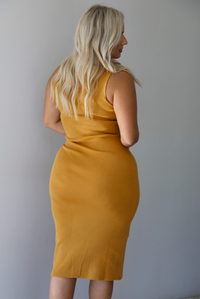 A woman shown from behind wearing a marigold sleeveless midi dress with a high, turtle neckline, ribbed textured material, and is fitted, standing indoors against a white wall.