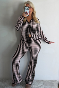 A woman taking a mirror selfie against a white wall wearing a light pink and brown two piece set consisting of a double zip hoodie top and mid-rise, wide leg pants. 