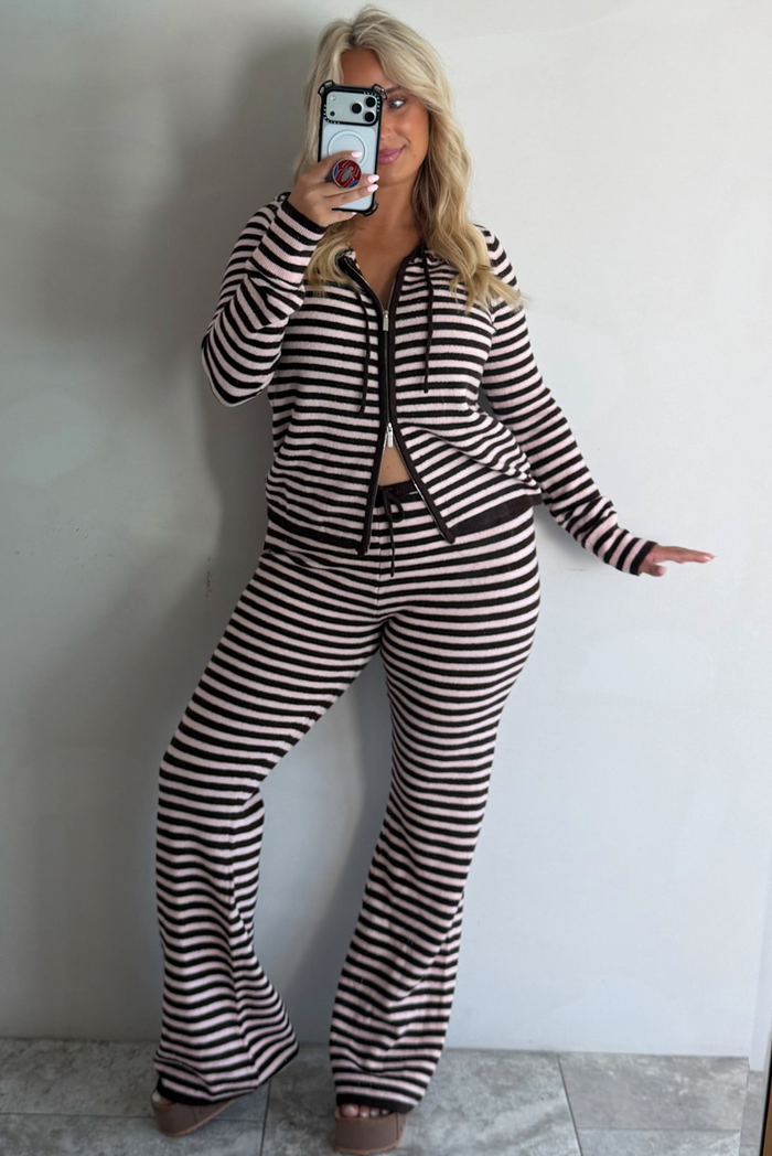 A woman taking a mirror selfie against a white wall wearing a light pink and brown two piece set consisting of a double zip hoodie top and mid-rise, wide leg pants. 