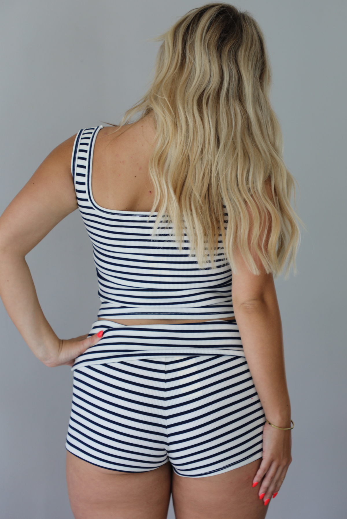 Woman wearing a navy and white striped two piece set with turquoise embellished star fish on the top and shorts indoors against a white wall. The photo shows a closeup of the back of the set.