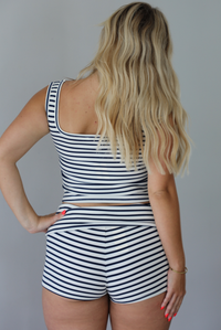 Woman wearing a navy and white striped two piece set with turquoise embellished star fish on the top and shorts indoors against a white wall. The photo shows a closeup of the back of the set.