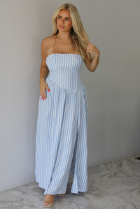 Woman wearing a blue and white striped strapless maxi dress indoors against a white wall with white marble flooring.