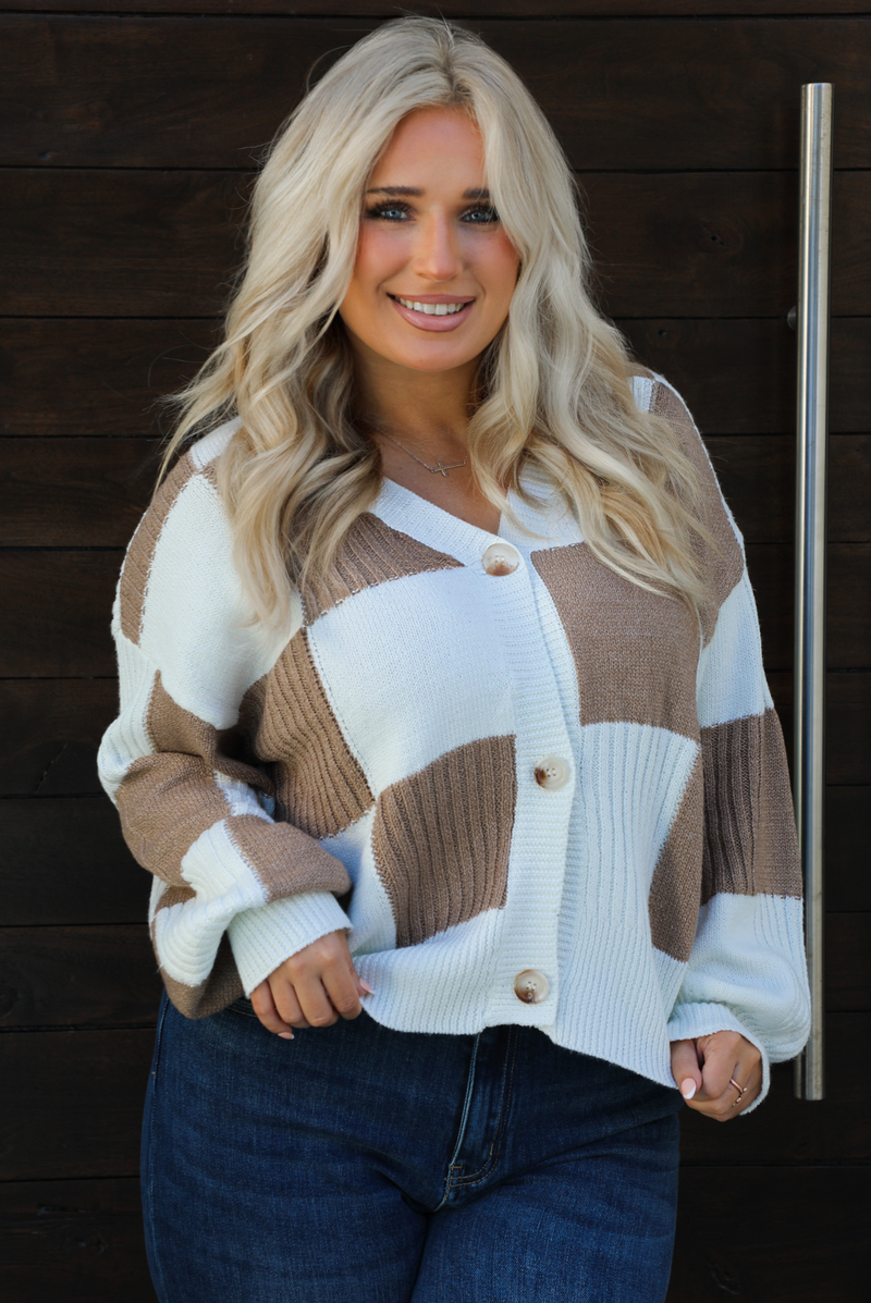 Close up of a woman model wearing a white and tan checkered patterned cardigan and dark wash denim. The cardigan has functional button closures in the front, is lightweight, and has a relaxed fit. 