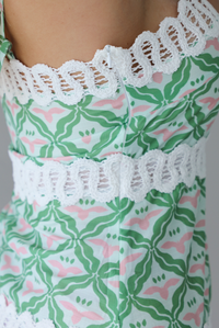 Woman wearing a teal, green, white, and pink dress with white lace trim detailing, thin, spaghetti straps, with a mini length design indoors against a white wall. The photo shows a closeup of the zipper closure on the side. 