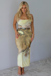 Woman wearing a yellow and brown floral print, strapless, fitted midi dress indoors against a white wall with white marble flooring. 