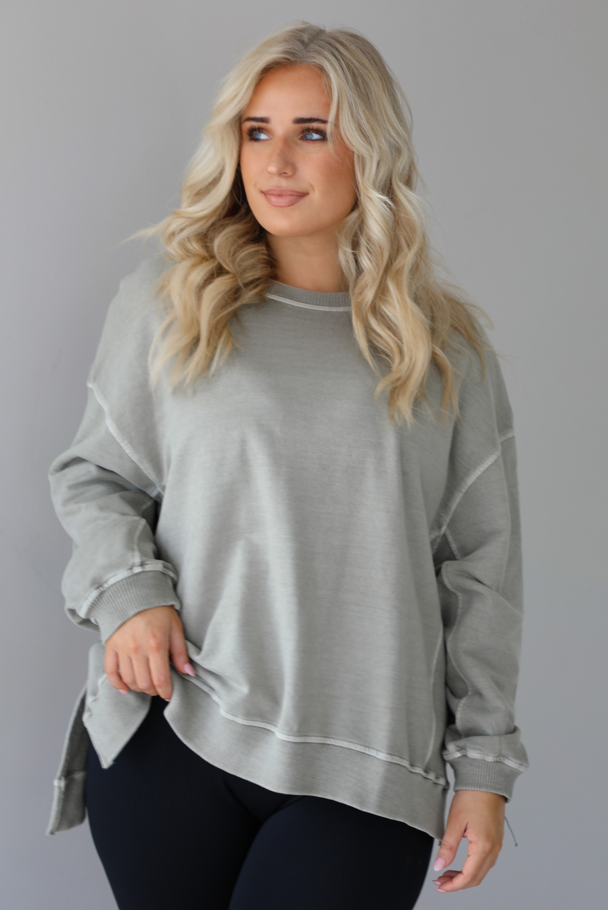 Woman wearing a tan oversized sweater with black leggings that have a slightly flared hem with split hem details in the front. The photo shows a closeup of the sweater and has a white background. 